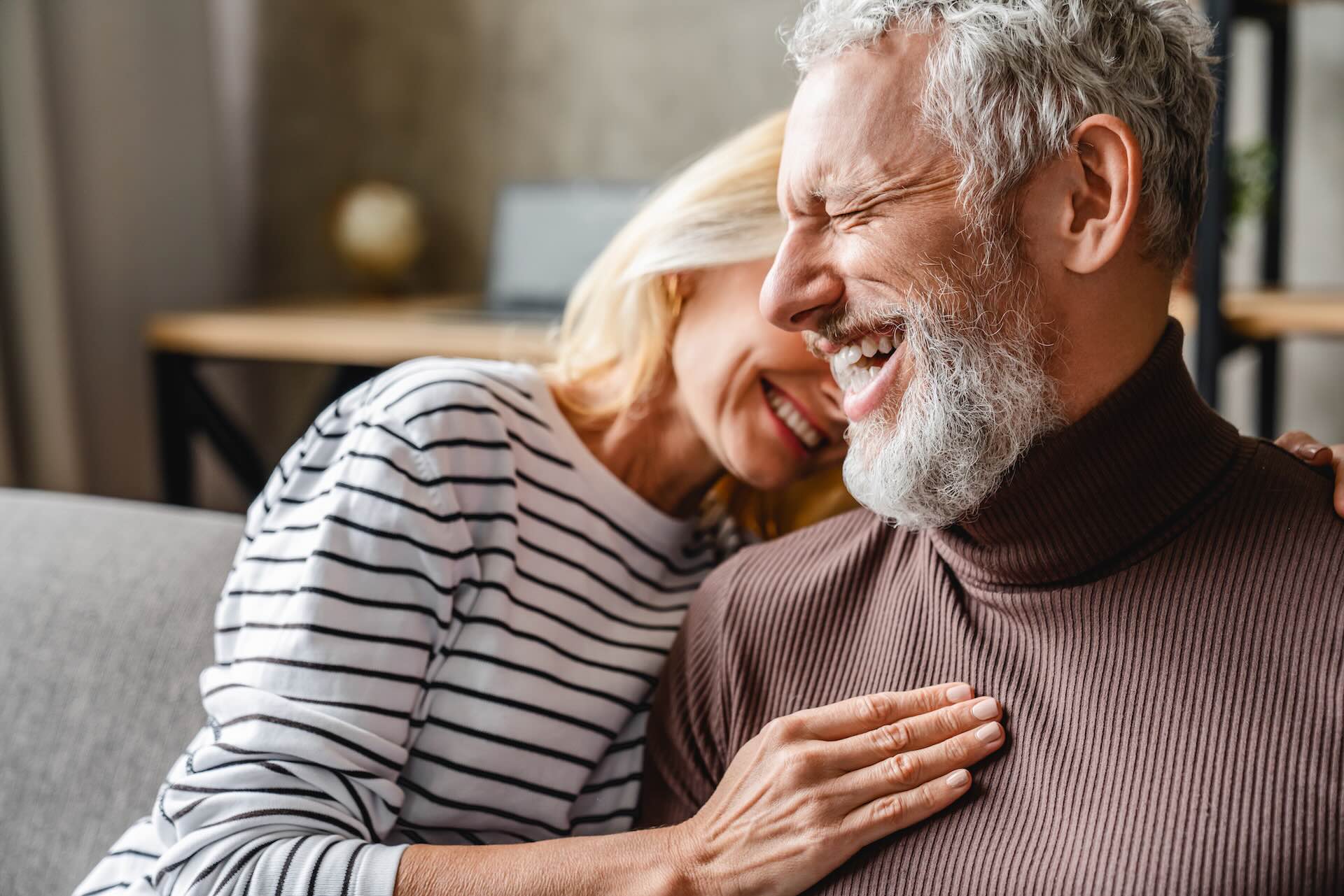 A mature couple smiling comfortably in their home